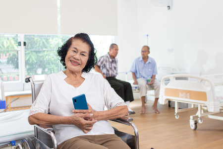 Portrait of senior woman using mobile phone while sitting in hospital corridorの写真素材