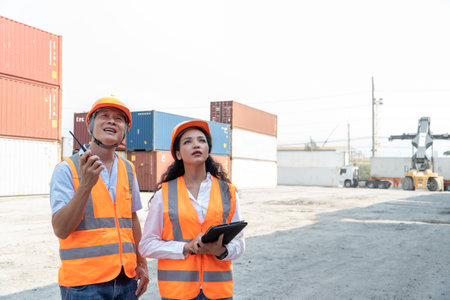 Portrait of Asian engineer man and woman wearing safety vests and holding digital tablet while standing at container yard.の写真素材