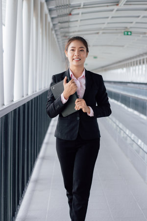 Businesswoman walking in the corridor of a modern office building with a laptopの写真素材