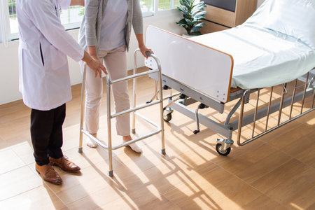 Doctor helping senior patient to walk on walker in hospital ward.の写真素材