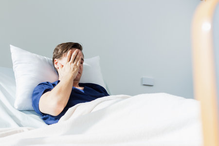 Man lying in bed covering his face with hands in ward at homeの写真素材