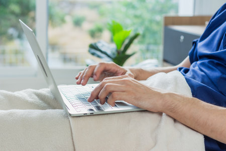Caucasian patient using laptop in hospital room. man sick patient lying in a hospital bed.の写真素材