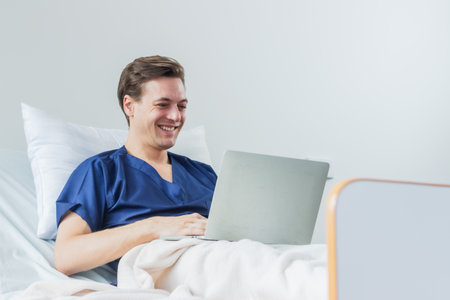 Caucasian patient using laptop in hospital room. man sick patient lying in a hospital bed.の写真素材