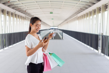 Portrait of young woman using mobile phone and holding shopping bag in the cityの写真素材