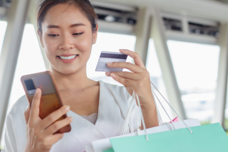 Smiling woman holding credit card and using mobile phone for online shoppingの写真素材