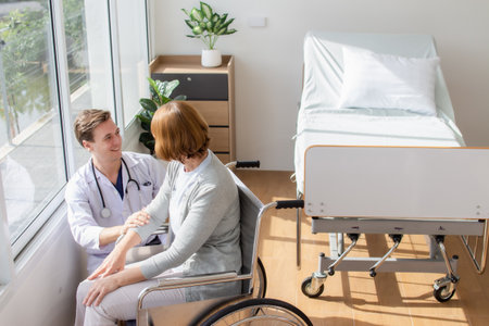 Doctor and senior patient discussing something while sitting in a wheelchair at the hospitalの写真素材