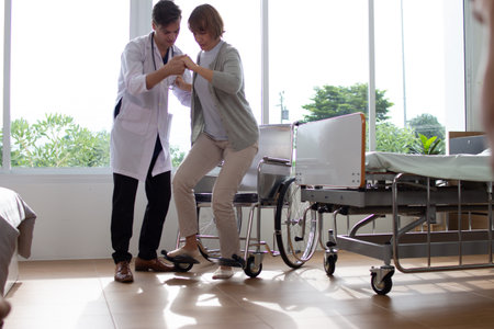 Doctor helping patient to use wheelchair in hospital room. Healthcare and medical concept.の写真素材