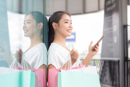 beautiful asian woman using mobile phone and shopping bag in mallの写真素材