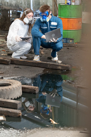 Two male and female workers in protective suits and masks working on a project in a factoryの写真素材
