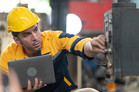 Caucasian male engineer in helmet working in industrial factory. Specialist engineer is using laptop...