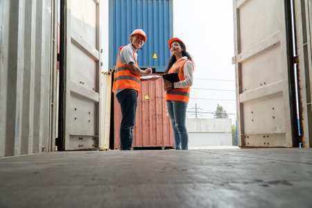 Two warehouse workers working together in freight cargo warehouse. Young Caucasian man and woman in hardhats and helmets.の写真素材