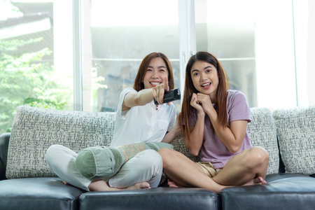 front view asian woman and friend sit at home on sofa bed watch tv movieの写真素材
