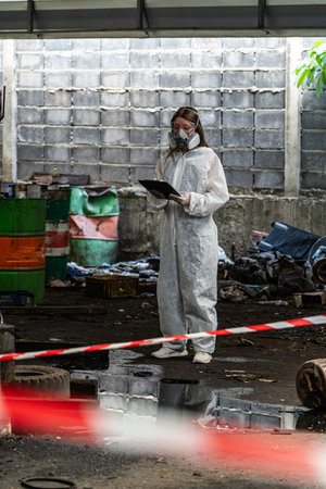 emergency pollution factory concept. Female chemist wearing PPE and gas mask inspecting oil on factory floor.の写真素材