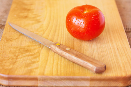 Red tomato and knife on a wooden chopping board