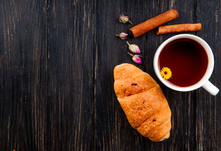 top view of a cup of tea with croissant and cinnamon sticks on black wooden background with copy spaceの写真素材