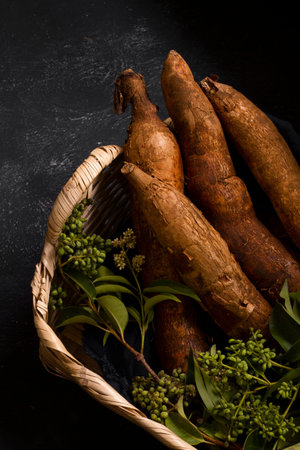 Raw taro roots in a wicker basket on a black background