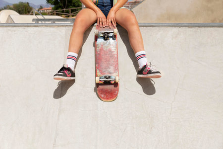 Skateboarder girl sitting on a skateboard in a skate park.