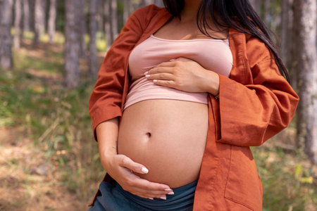 Close-up of pregnant woman touching her belly in the forest.の写真素材