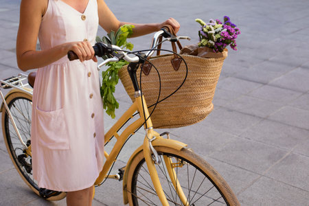 Cropped view of woman in dress riding bicycle with basket of flowers on streetの写真素材