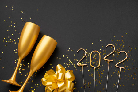 Happy New Year 2022. Gold champagne glasses and golden confetti on black background, flat lay. Space...