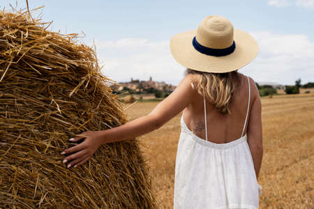back view of woman in straw hat looking at haystack in fieldの写真素材