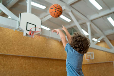 Little boy with curly hair playing basketball at the gym, back viewの写真素材