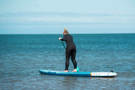 Young woman in wetsuit standing on stand up paddle board.