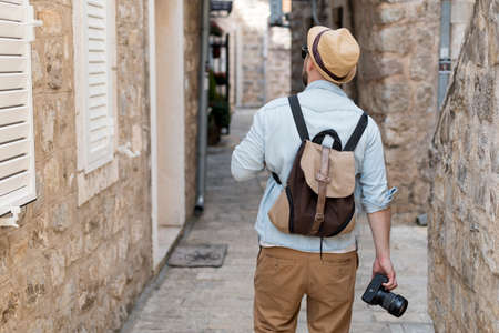 Back view of a man with a camera in his hands walking through the old townの写真素材
