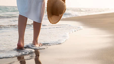Woman walking barefoot on the beach at sunset, closeup. Space for textの写真素材