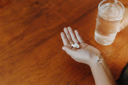 medicine in her hand with a glass of water on a wooden table, Take a medicineの写真素材