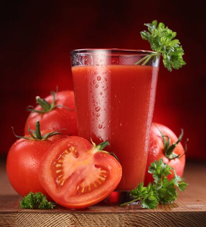 Juice tomato and fresh tomatoes with parsley on table red background.の写真素材