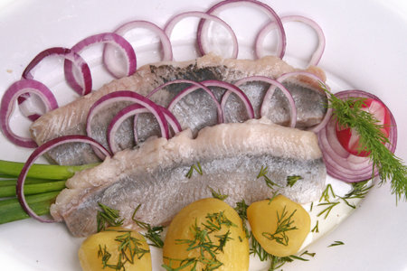 Herring fillet fish potatoes boiled onion greens on a white background.