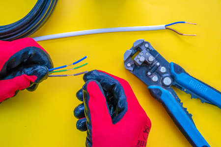 Electrician peeling off insulation from wires - closeup on hands and pliersの写真素材