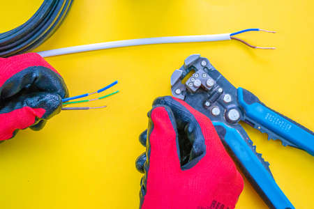 Electrician peeling off insulation from wires - closeup on hands and pliersの写真素材