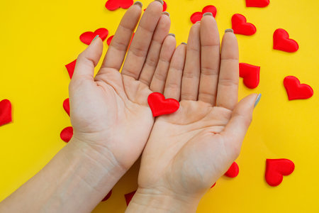 Hands on a yellow background with a heart, love. Selective focus.の写真素材