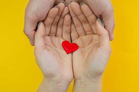 Hands on a yellow background with a heart, love. Selective focus.の写真素材