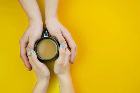 Hands on a yellow background with coffee, love. Coffee with milk, black cup. Selective focus.の写真素材