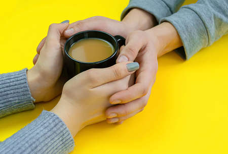 Hands on a yellow background with coffee, love. Coffee with milk, black cup. Selective focus.の写真素材