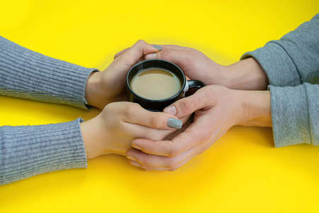 Hands on a yellow background with coffee, love. Coffee with milk, black cup. Selective focus.の写真素材
