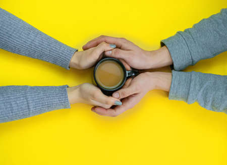 Hands on a yellow background with coffee, love. Coffee with milk, black cup. Selective focus.の写真素材