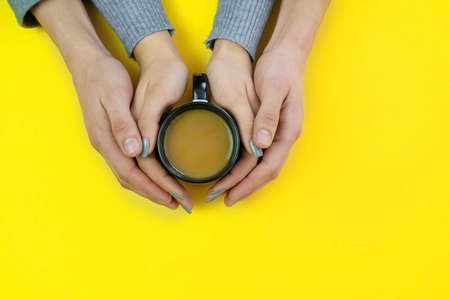 Hands on a yellow background with coffee, love. Coffee with milk, black cup. Selective focus.の写真素材