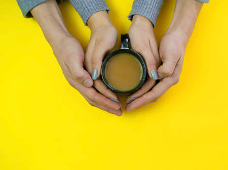 Hands on a yellow background with coffee, love. Coffee with milk, black cup. Selective focus.の写真素材