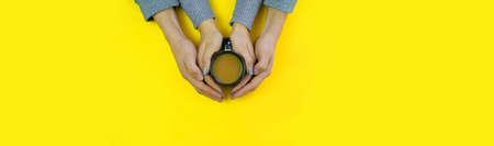 Hands on a yellow background with coffee, love. Coffee with milk, black cup. Selective focus.の写真素材