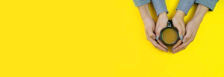Hands on a yellow background with coffee, love. Coffee with milk, black cup. Selective focus.の写真素材