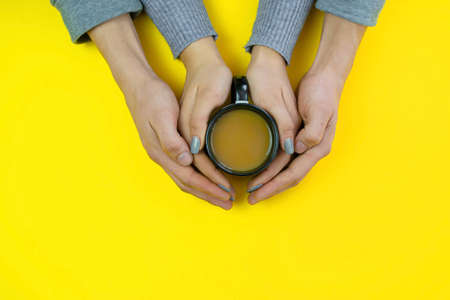 Hands on a yellow background with coffee, love. Coffee with milk, black cup. Selective focus.の写真素材