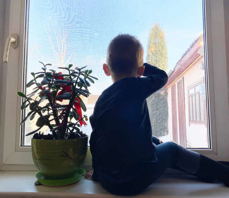the child looks out the window and waits for parents from work. Selective focus.の写真素材