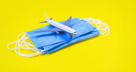 Hand in glove holding model airplanes on yellow background. Airplane model on hand and face medical mask Concept traveling.の写真素材