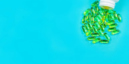 Omega 3 fish oil capsules spilling out of a bottle on a blue background.の写真素材