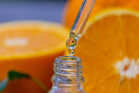 Essential orange oil in a bottle, fresh fruit pieces on the background. Natural flavors. Selective...
