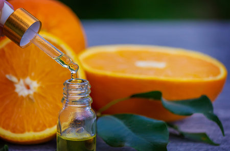 Essential orange oil in a bottle, fresh fruit pieces on the background. Natural flavors. Selective...